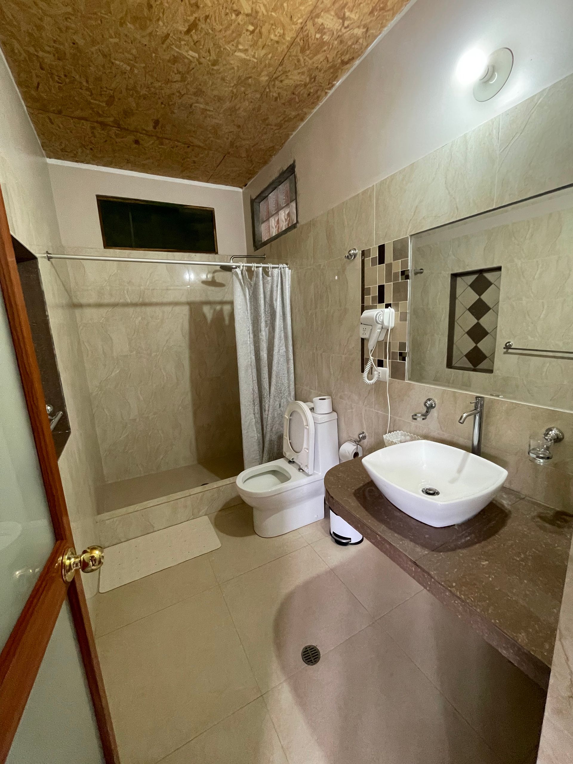 Baño pequeño con cabina de ducha, inodoro y lavabo, paredes y suelo de azulejos beige.