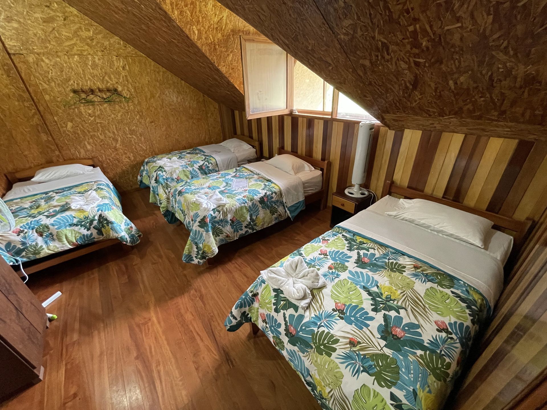 Pequeña habitación abuhardillada con tres camas individuales, paredes revestidas de madera y techo inclinado.
