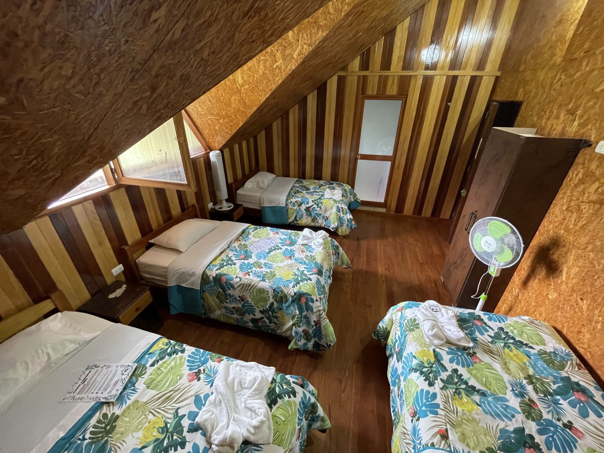 Pequeña habitación abuhardillada con cuatro camas individuales, paredes revestidas de madera y techo inclinado.