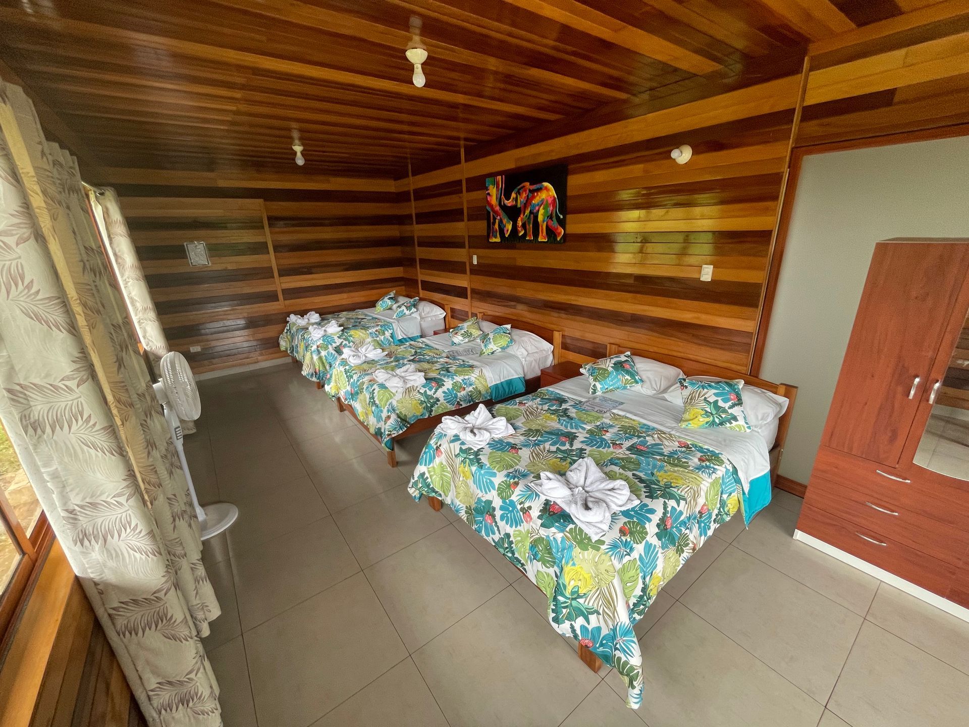 Pequeña habitación de madera con dos camas individuales cubiertas con ropa de cama de estampado floral azul verdoso.