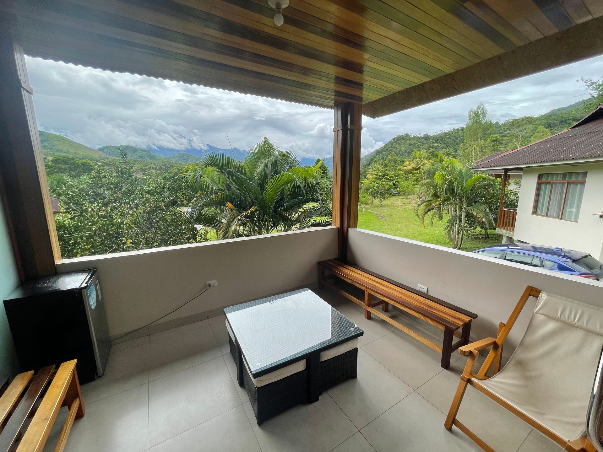 Porche cubierto con bancos y mesa de madera con vistas a un valle verde exuberante y a la casa vecina.