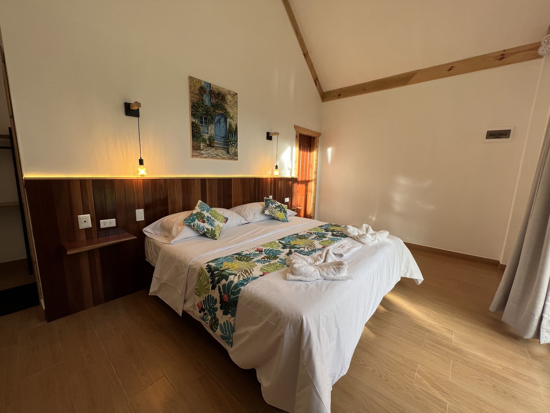 Acogedora habitación con cama doble, paredes revestidas de madera, lámparas cálidas y cortinas claras.