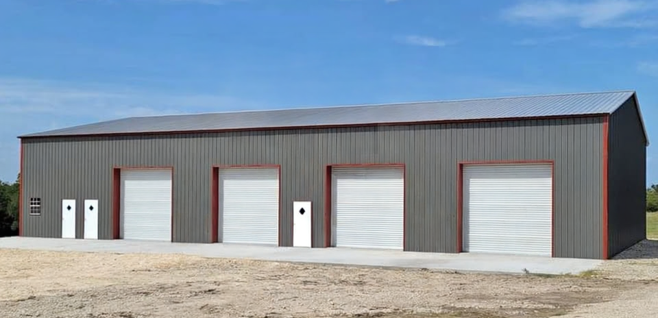 A grey metal building with four white garage doors and three white entry doors under a blue sky.