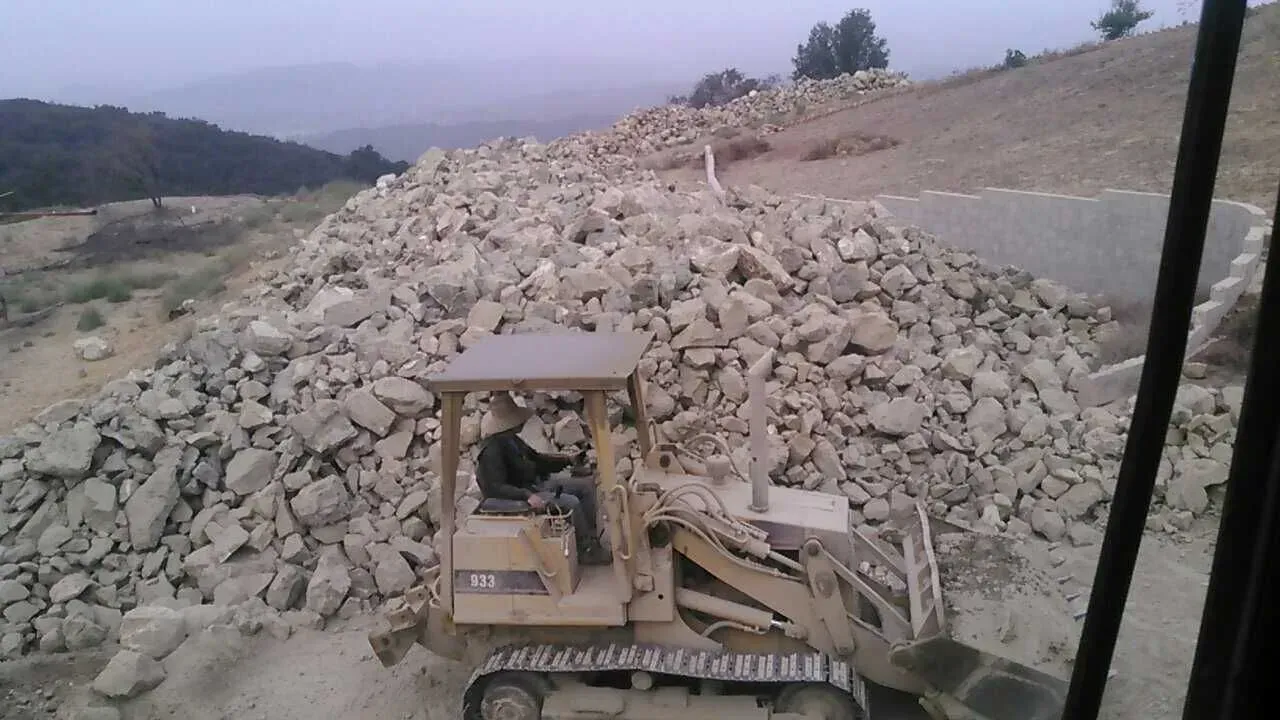 A bulldozer pushing a large pile of rocks on a hillside.