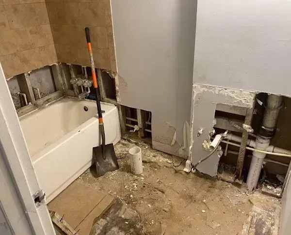Bathroom demolition in progress: tub, exposed walls, shovel, debris.