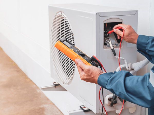 HVAC technician using multimeter on an outdoor air conditioning unit, testing electrical components.