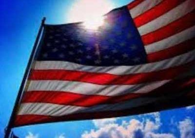 American flag waving against a bright sun and blue sky.