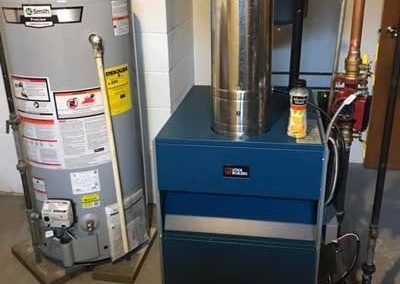 Water heater and blue boiler in a utility room. Chimney pipe rises from boiler.