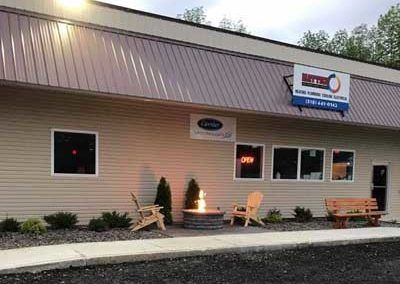 Exterior of a business with metal roof, windows, fire pit, and Adirondack chairs. Sign reads