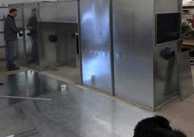 Person assembling large metal structures indoors. Metal sheets and dog visible.