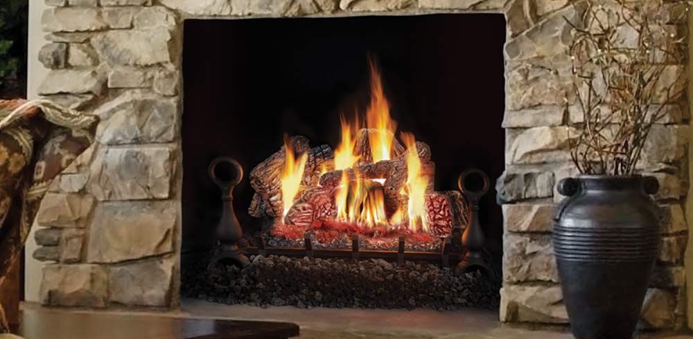 Fire pit with flames, flanked by evergreens, against a light-colored siding wall.