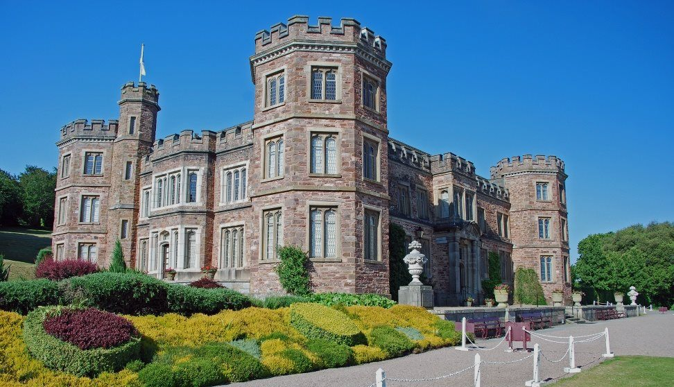 Stone castle with turrets and manicured gardens under a clear blue sky.