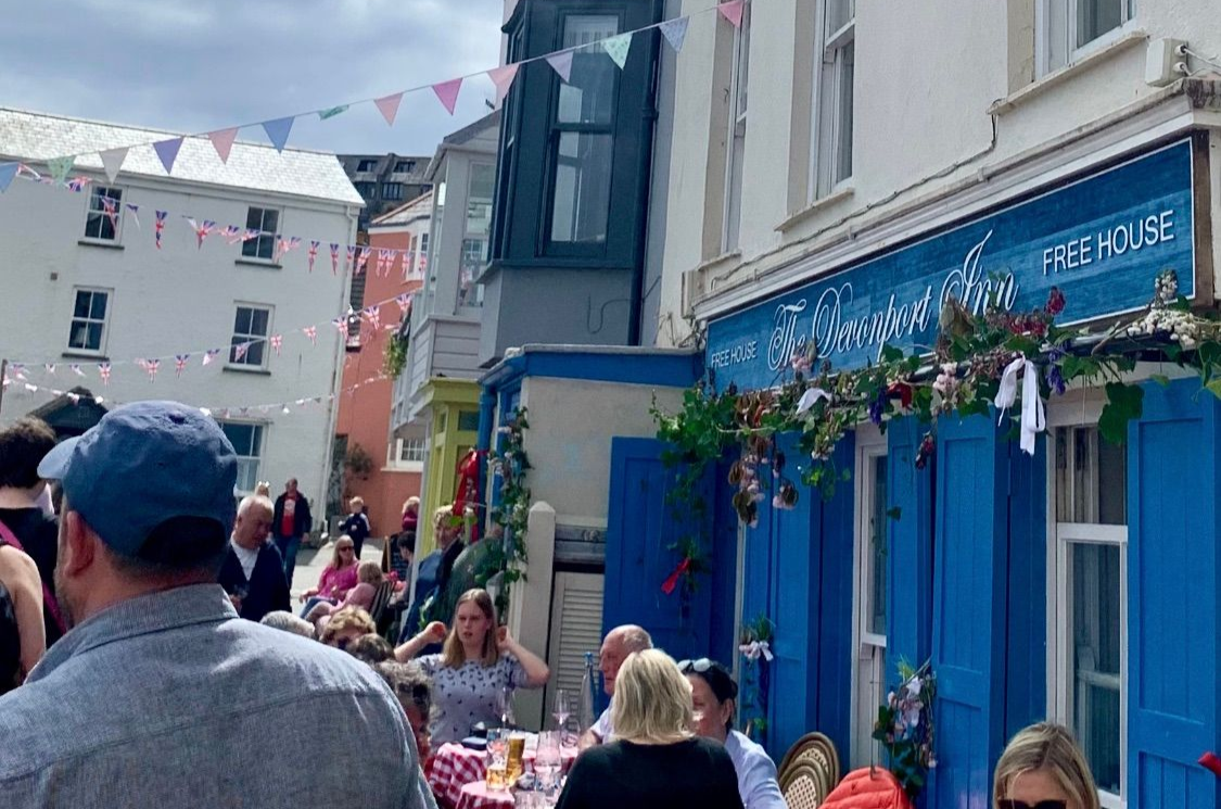 Street scene with a cafe, blue shutters, and people dining outdoors under bunting.