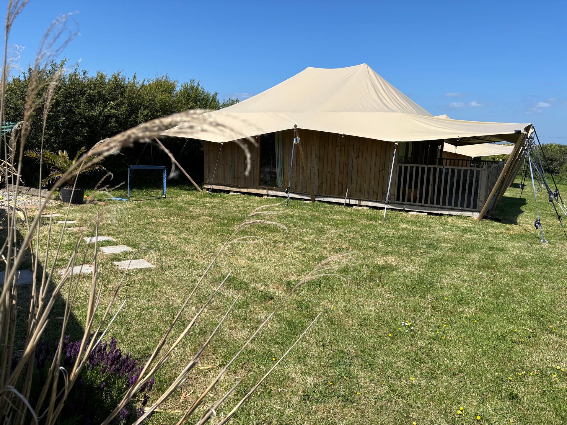 Beige glamping tent on a grassy lawn with a blue sky.