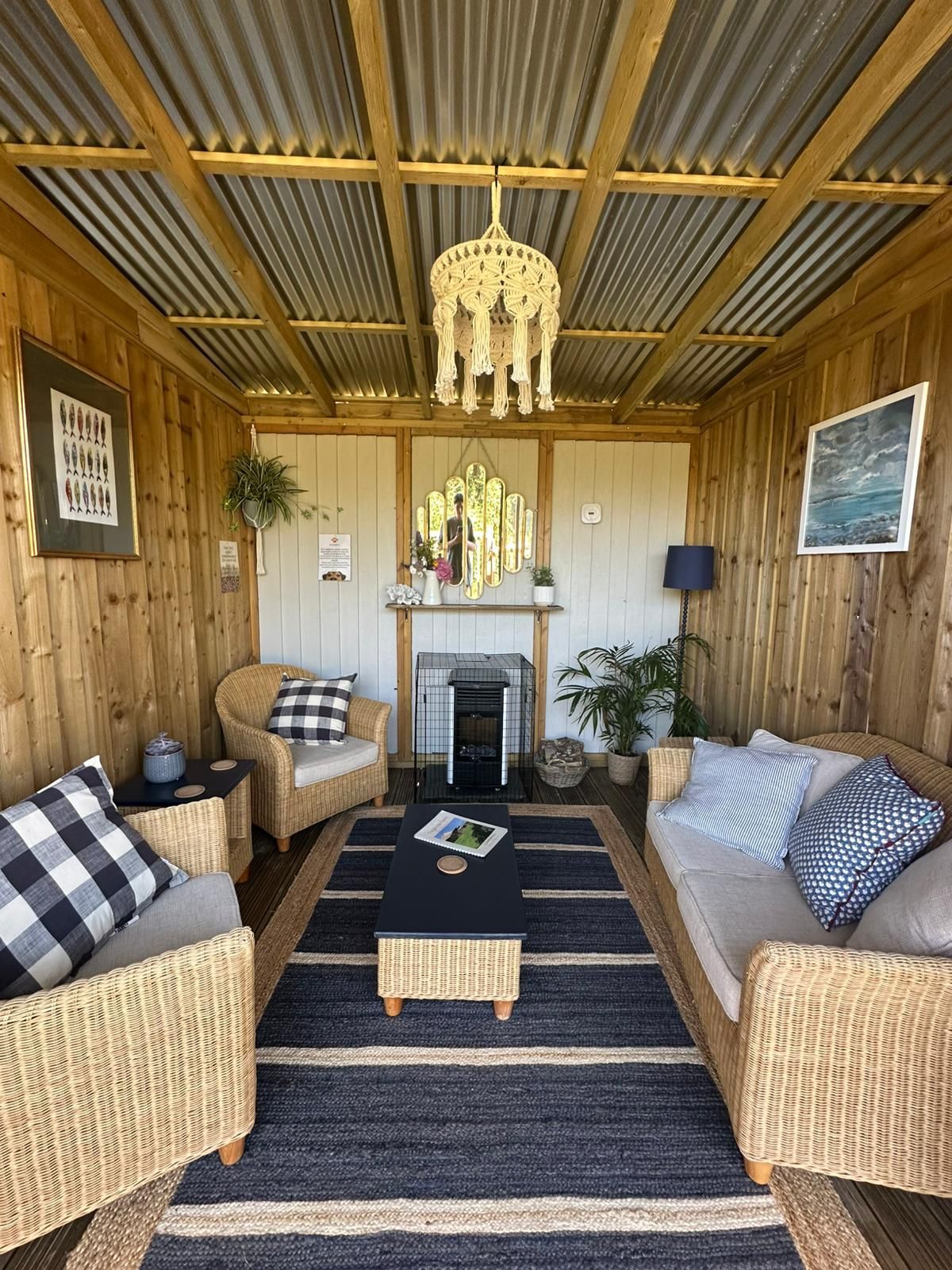 Cozy outdoor room with wicker furniture, a rug, and a macrame chandelier. Wooden walls and a metal roof.
