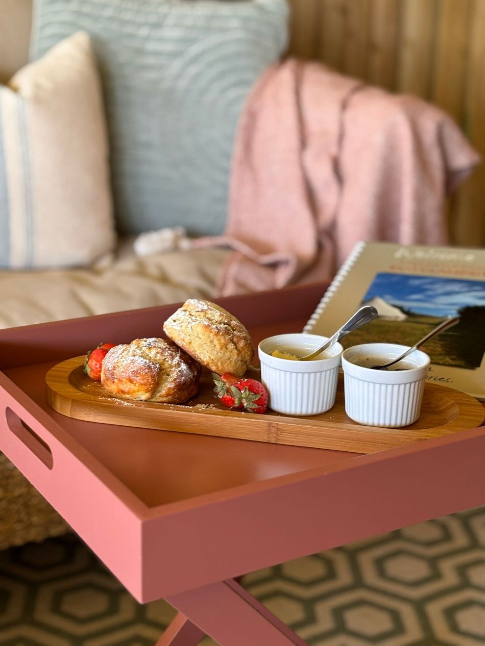 Breakfast tray with pastries, strawberries, and sauces on a pink table, set near pillows and a blanket.