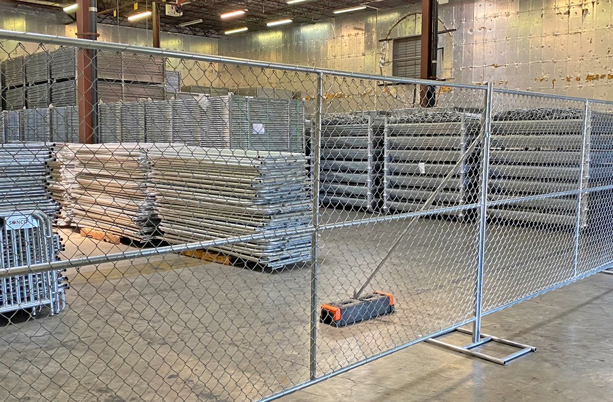 Chain-link fence in a warehouse, with stacks of metal objects visible behind it, along with a tool.
