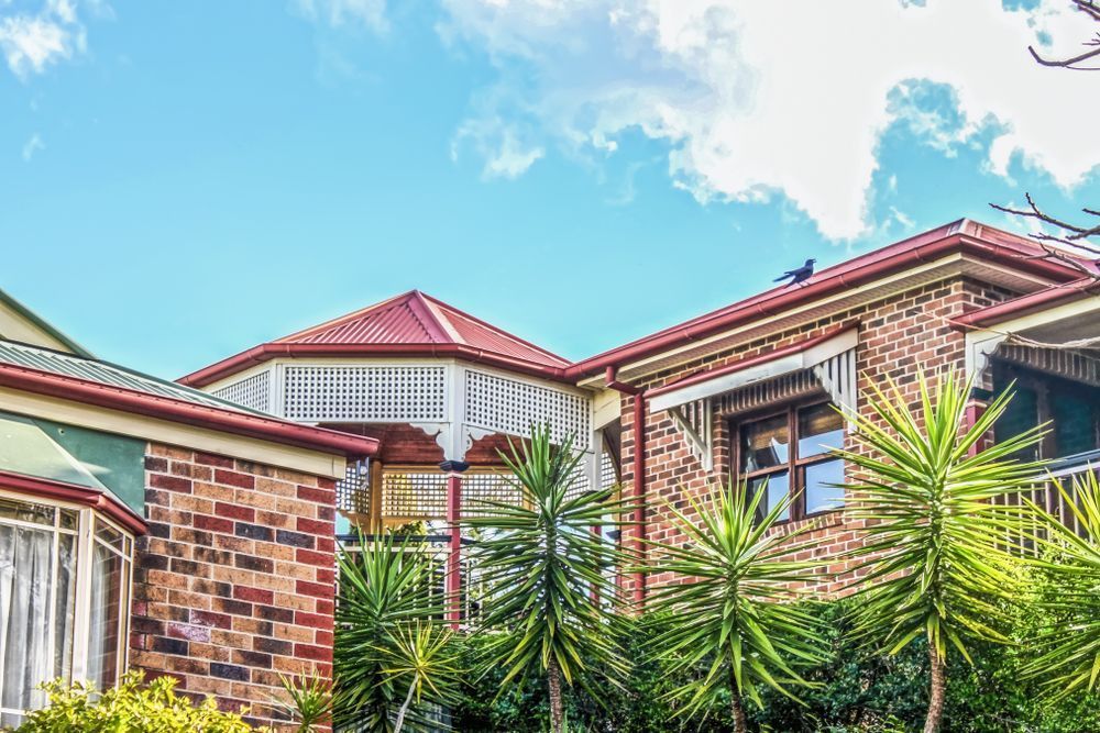 A Large Brick House With a Red Roof and Palm Trees in Front of It — Monty's Metal Roofing In Brunswick Heads, NSW