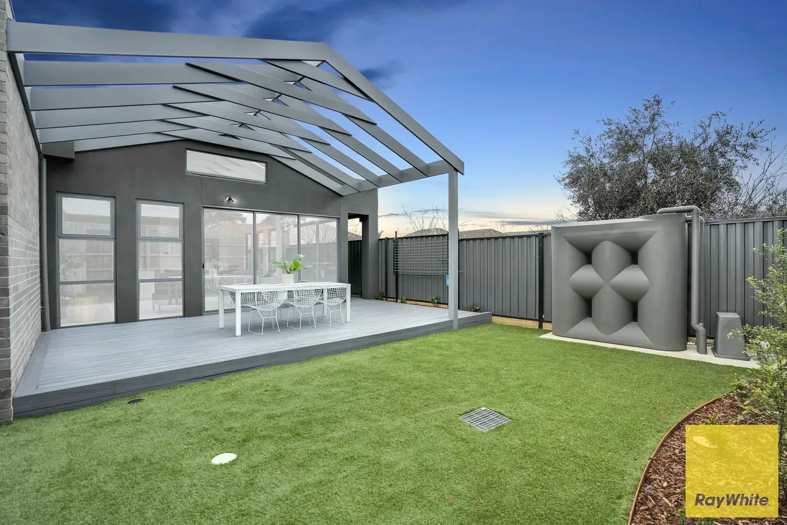 Modern backyard patio with pergola, outdoor dining table, green lawn, and privacy fencing