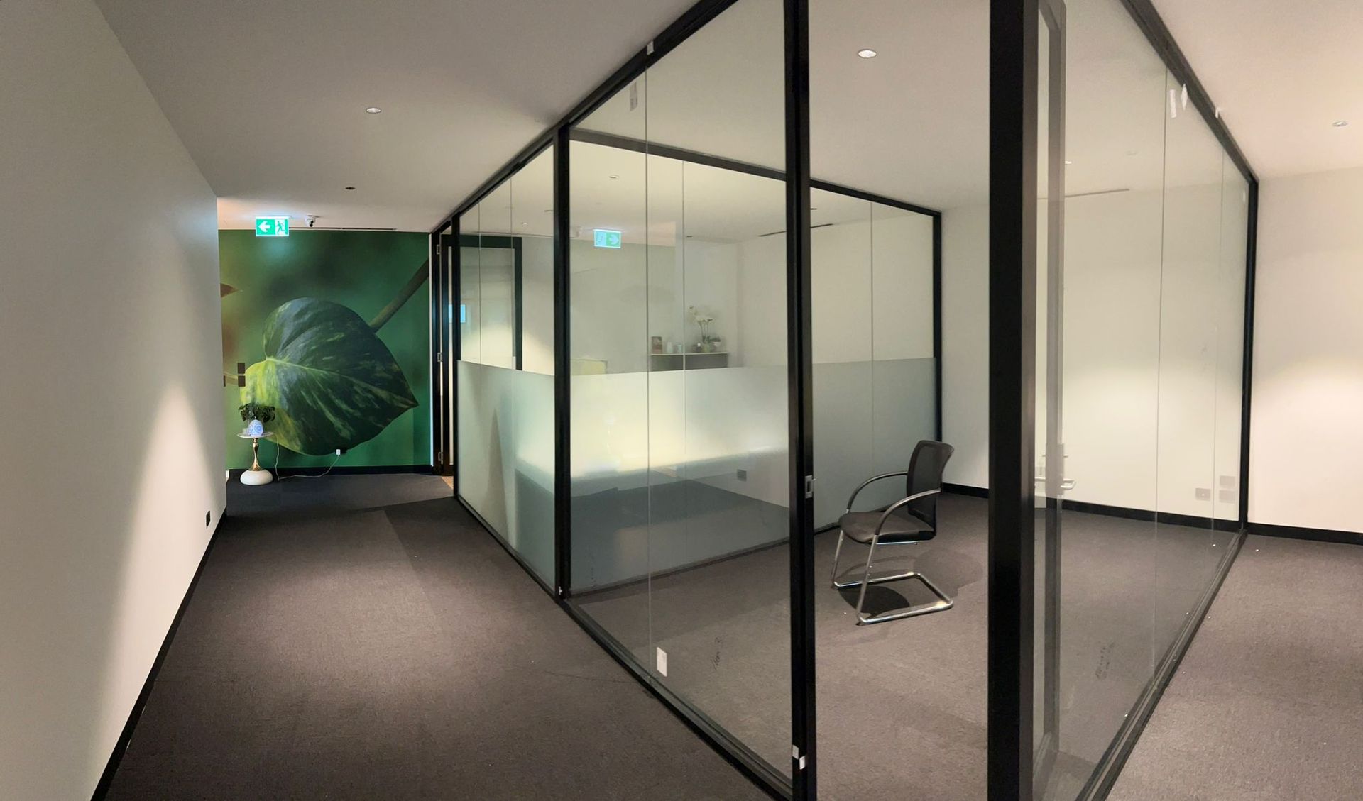 Modern office hallway with glass-walled meeting rooms and black chairs inside