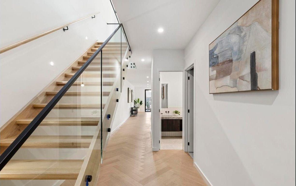 Modern hallway with wooden stairs, glass railing, white walls, and abstract wall art