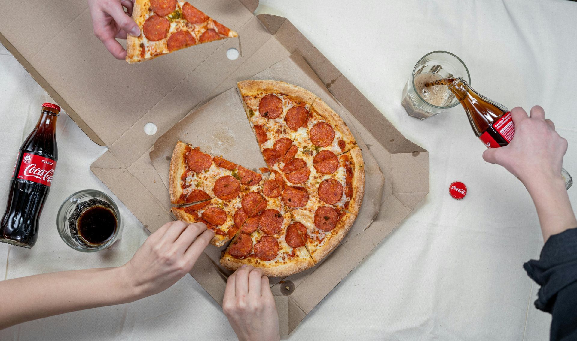 Pizza with pepperoni and soda in glasses and bottles; people eating.