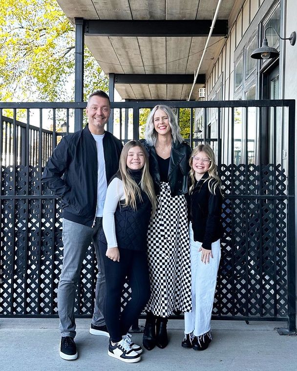 Family of four standing outdoors in front of a black gate, smiling at the camera.