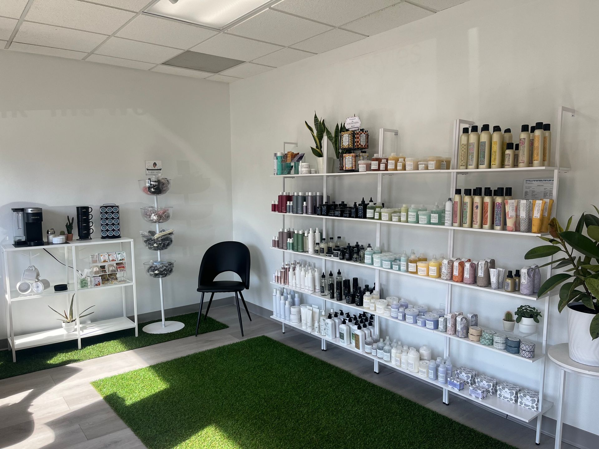 Bright salon room with shelves of products, a black chair, and a green rug near a window