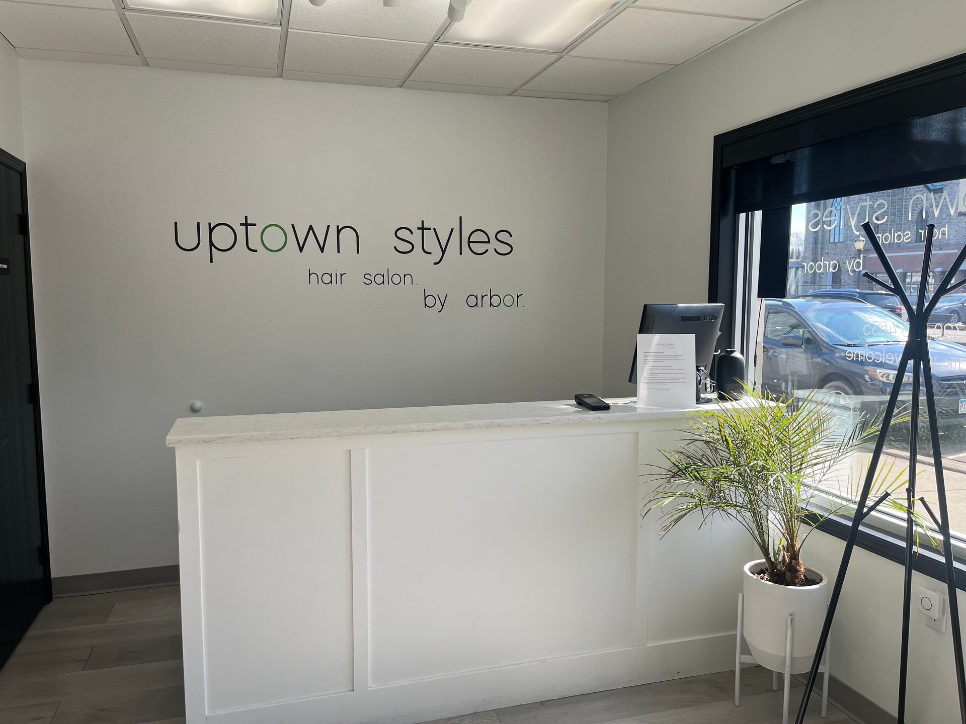 Modern salon reception desk with “uptown styles” wall sign and a potted plant by the window