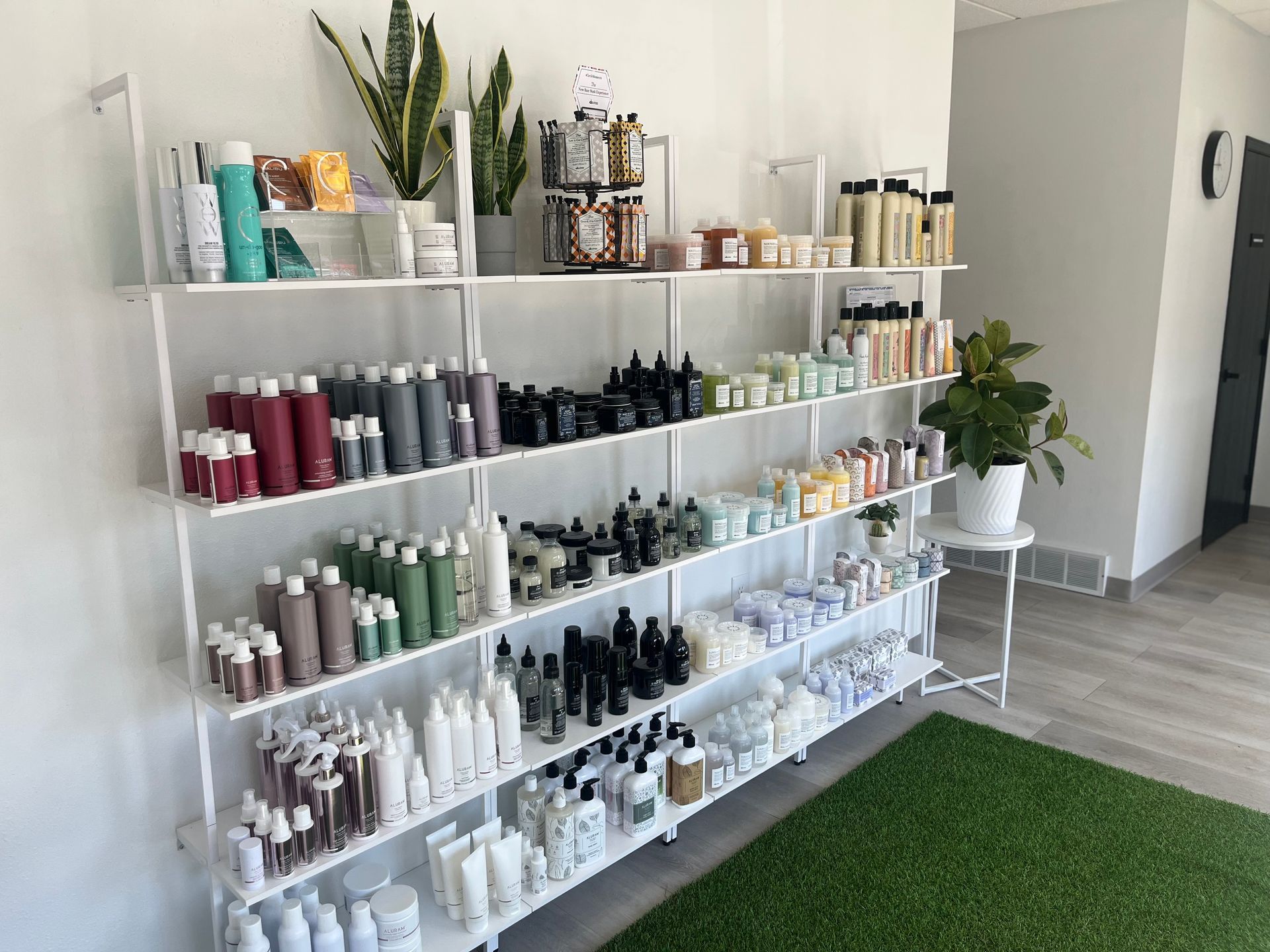 White shelving stocked with hair and beauty products in a bright salon room with wood floor and green rug