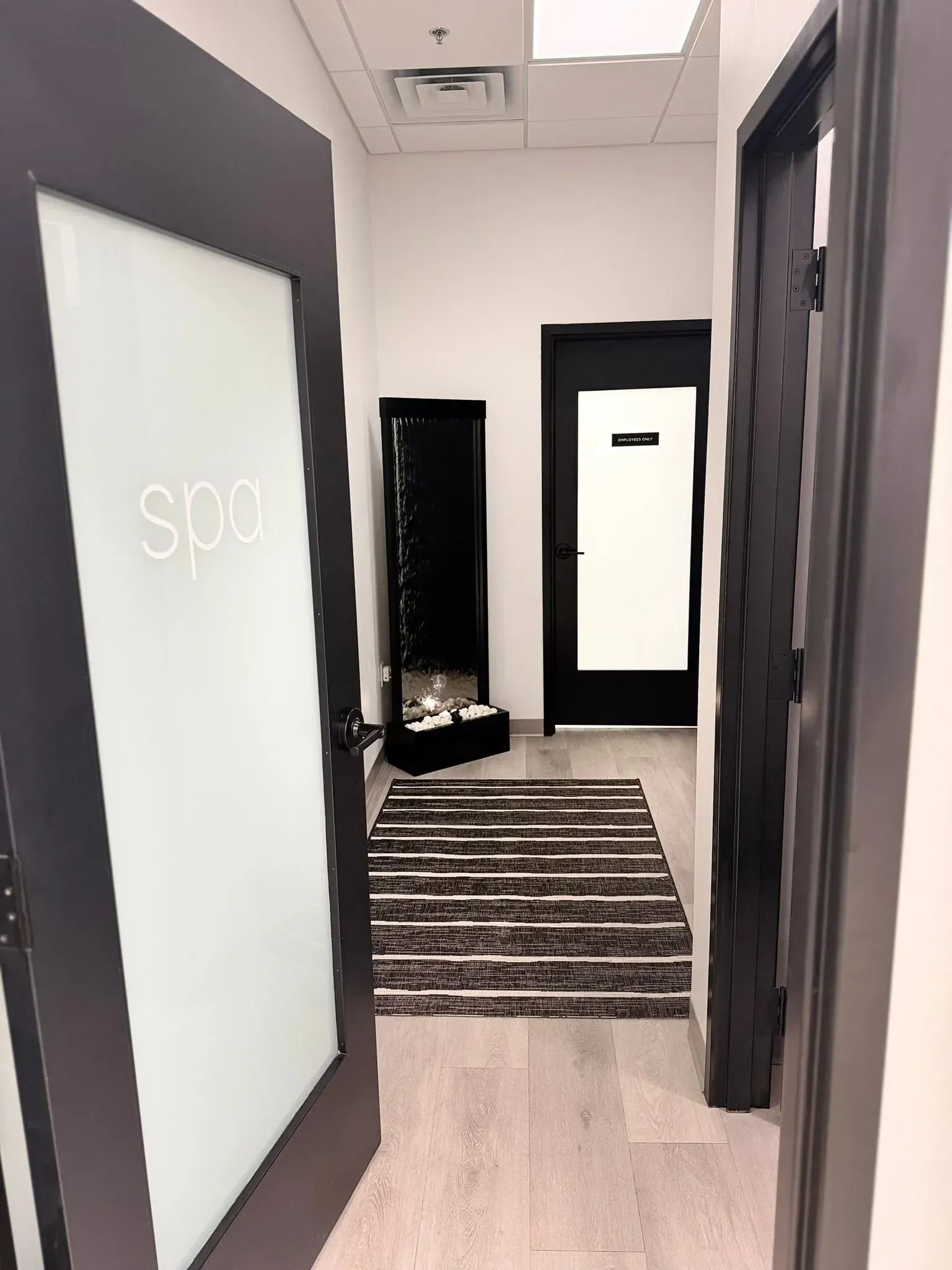 Office hallway with dark doors, striped rug, and a full-length mirror at the end.