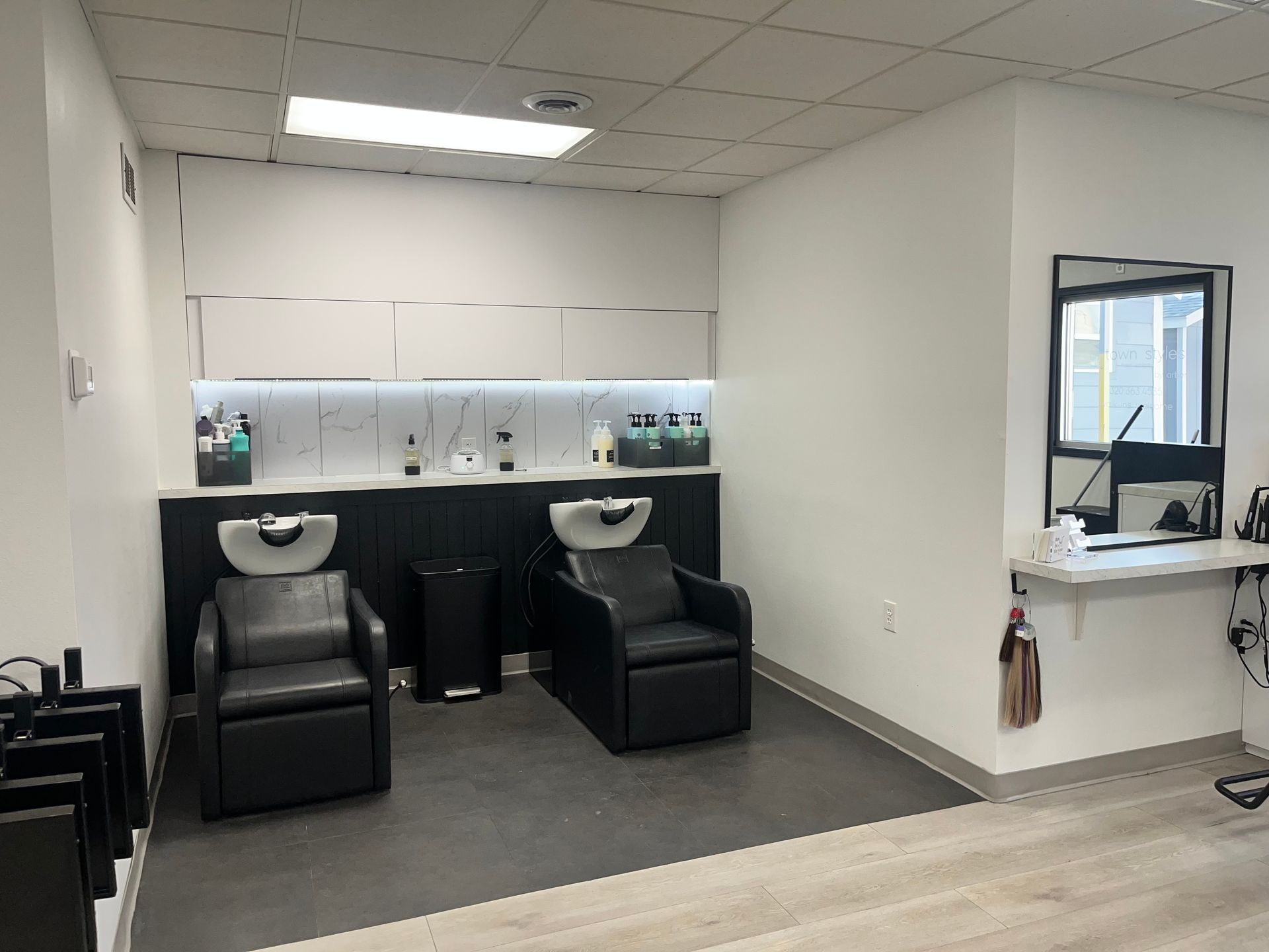 Hair salon wash station with two black shampoo chairs and a white shelf in a minimalist room