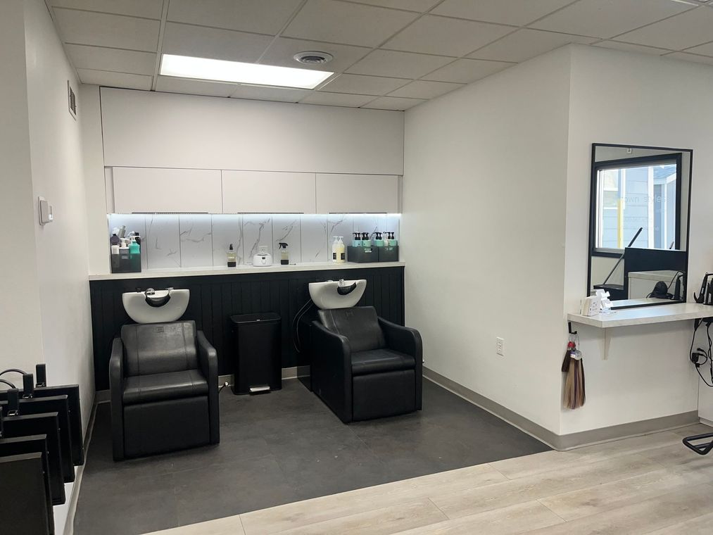 Hair salon wash station with two black shampoo chairs and a white shelf in a minimalist room