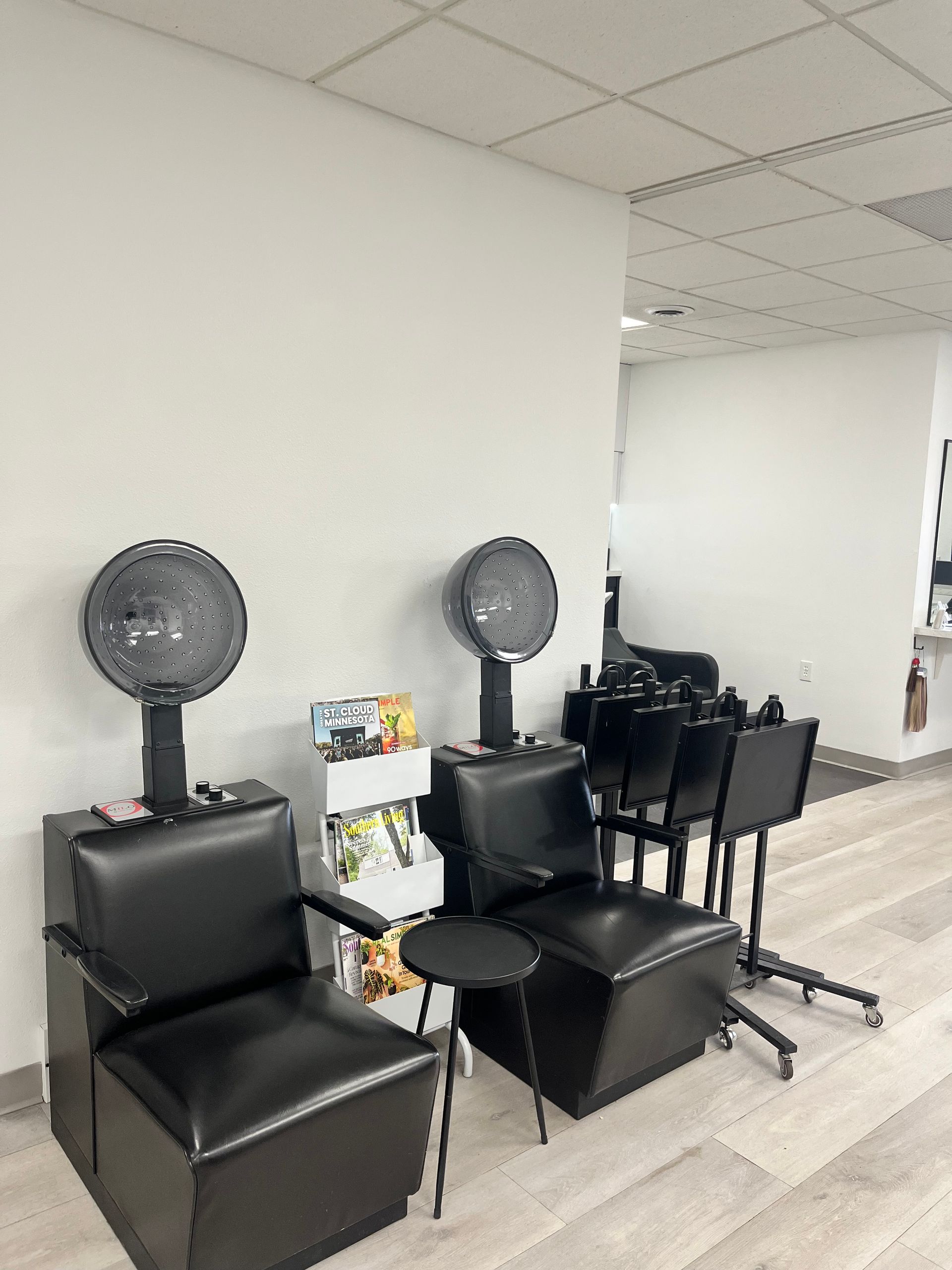 Salon waiting area with black chairs and standing fans against a white wall
