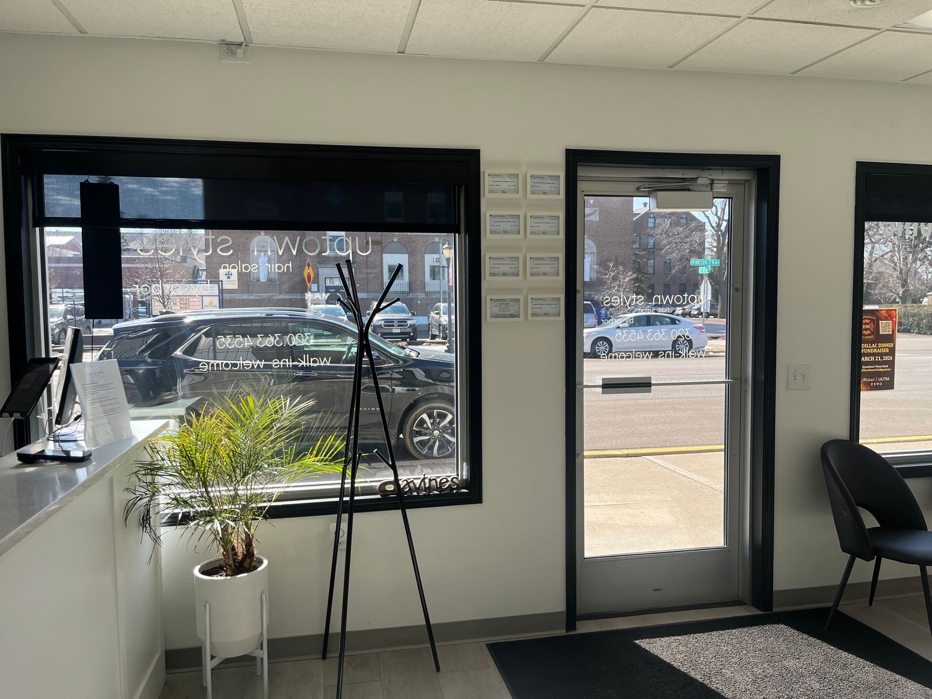 Bright storefront interior with window view, glass door, potted plant, and chairs.
