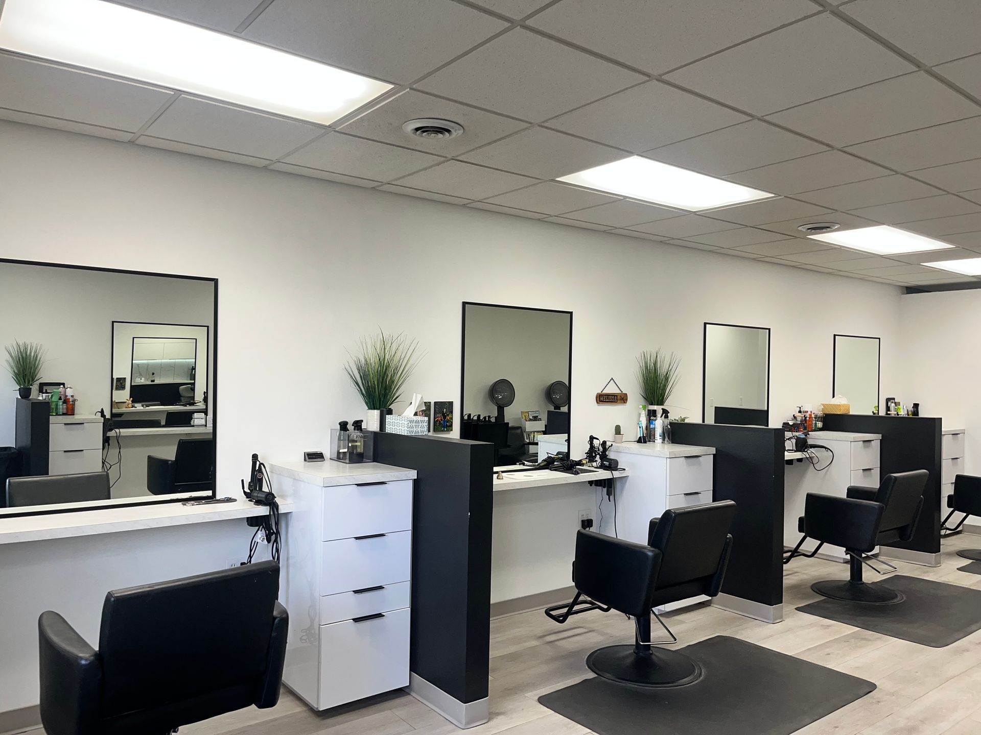 Empty hair salon with styling stations, mirrors, chairs, and white cabinets under bright ceiling lights
