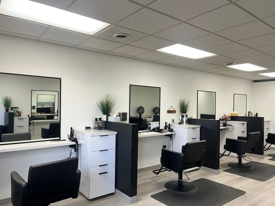 Empty hair salon with styling stations, mirrors, chairs, and white cabinets under bright ceiling lights