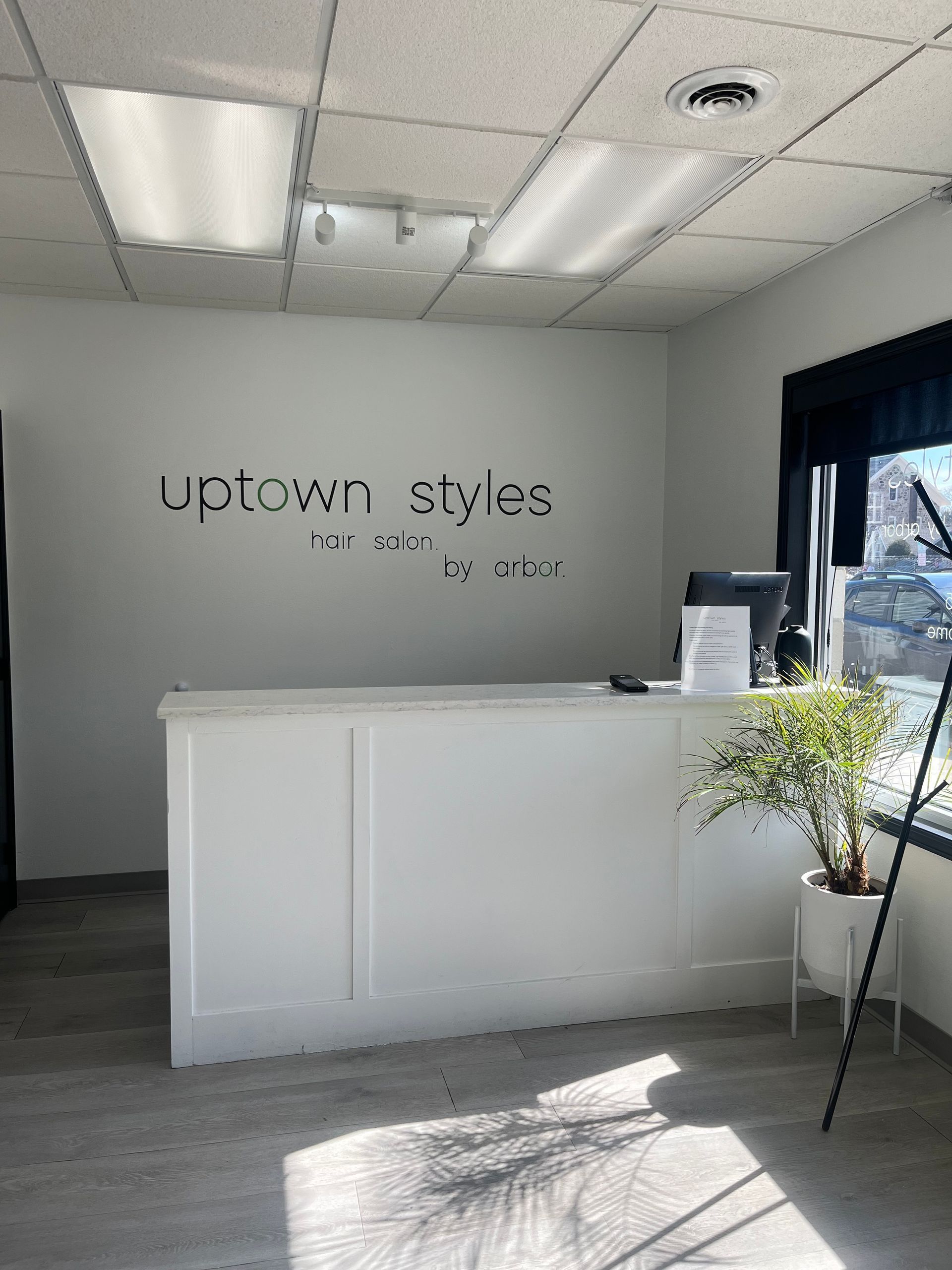 Bright salon reception area with white desk, “UpTown Styles” sign, and sunlight by the window.