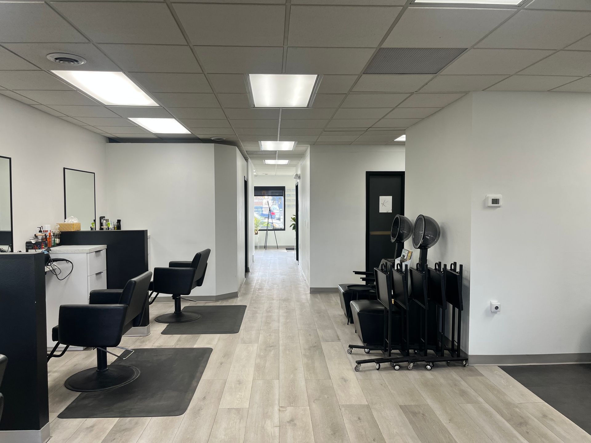Modern salon interior with styling stations, black chairs, and a hallway leading to the back.