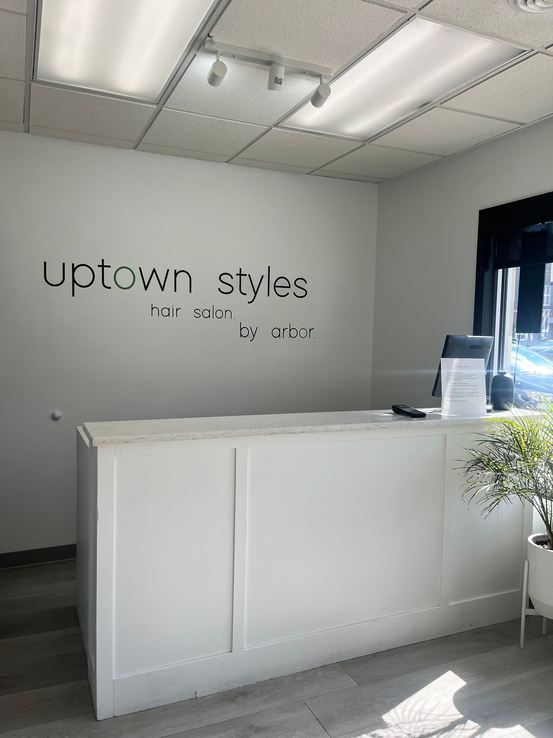 Modern white salon reception desk in a bright lobby with “Uptown Styles” sign on the wall.