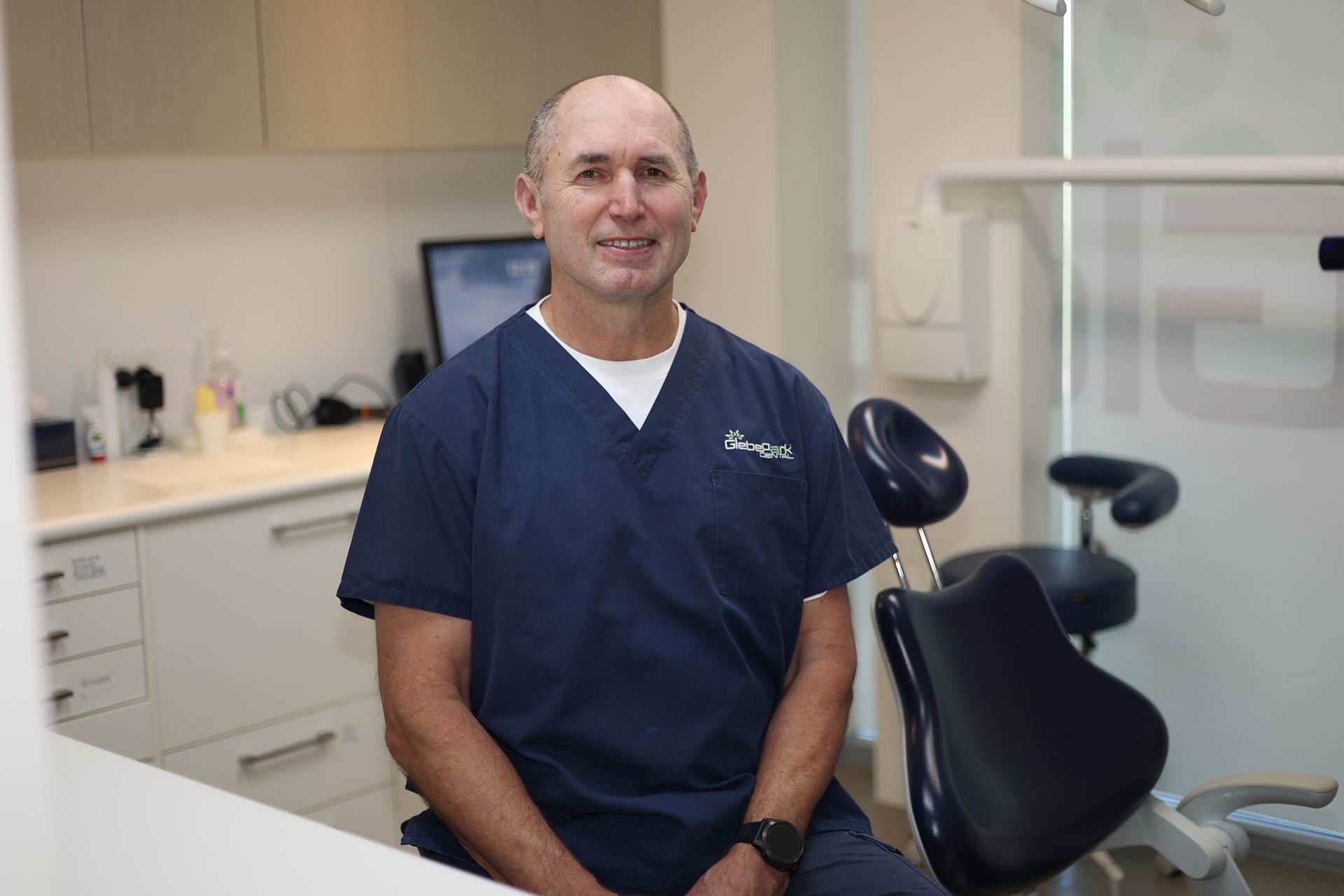 Dentist examining a smiling patient in a dental chair, holding a mirror, wearing blue gloves