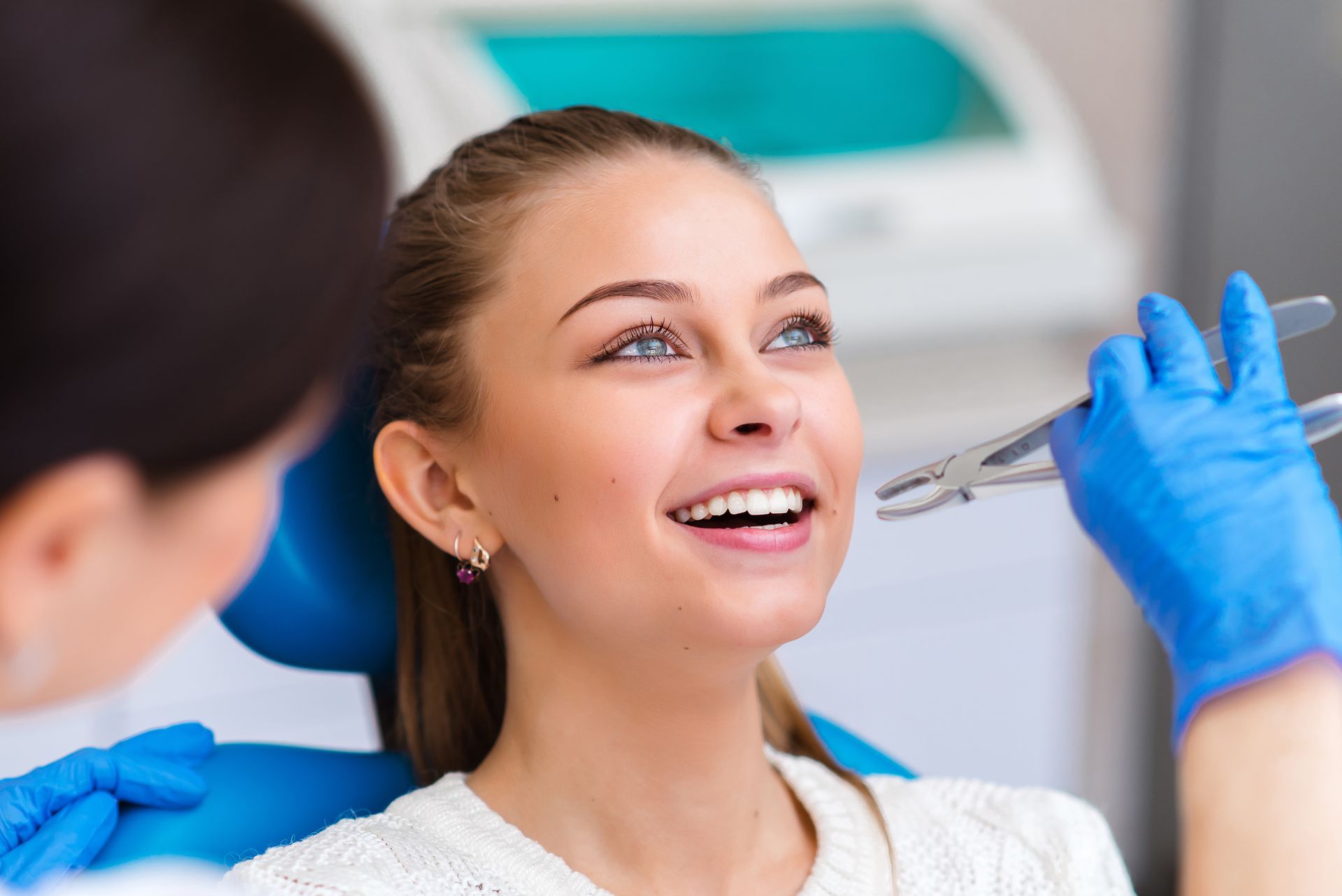 Patient smiling as a dentist examines teeth with blue-gloved hands in a bright clinic