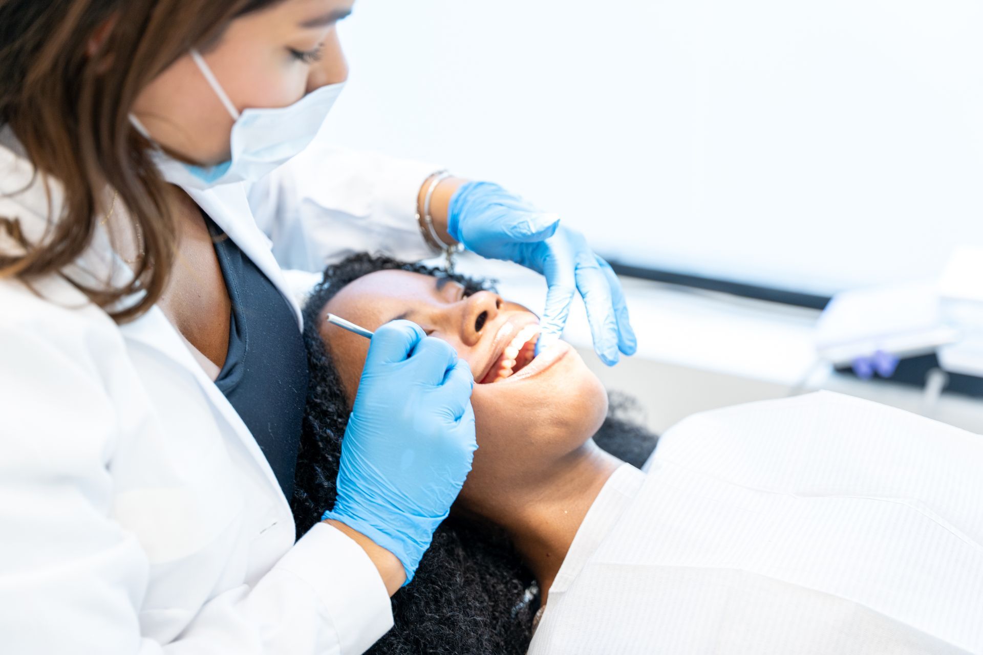 Dentist in blue gloves examining a patient’s teeth in a dental chair