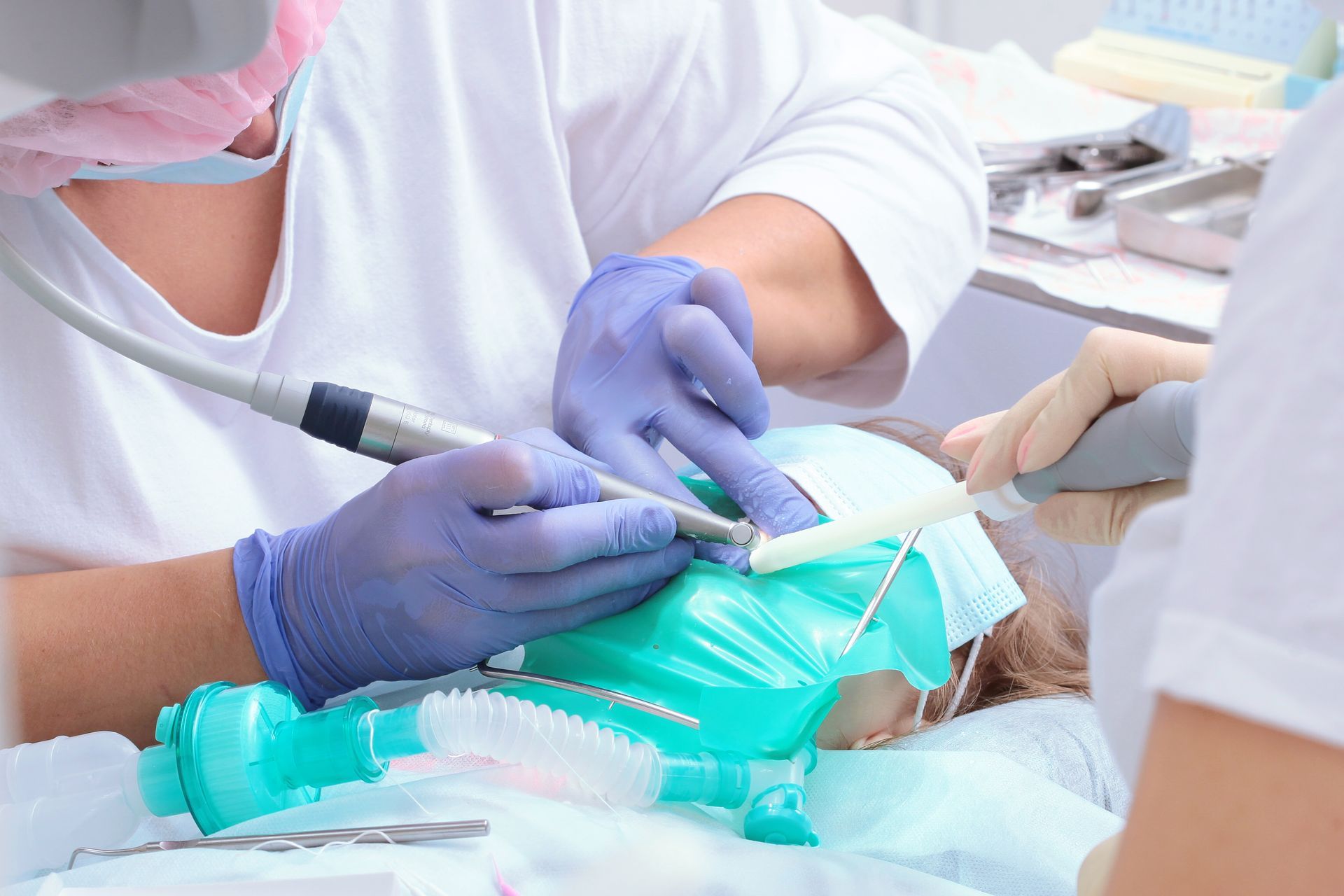 Dental team treating a patient, using a blue mask and dental tools in a clinic.