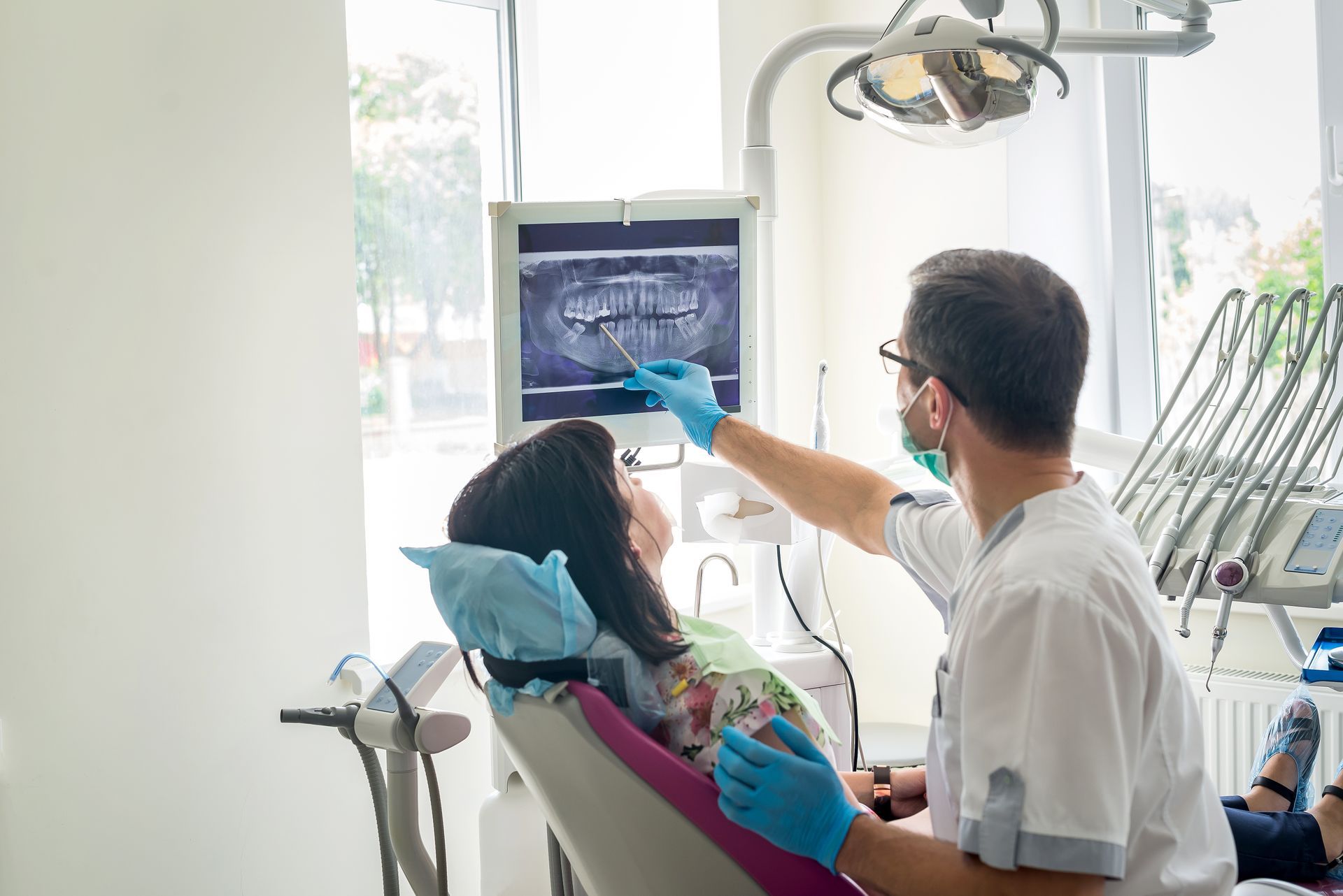 Dentist examining patient’s teeth in a bright dental clinic using an overhead monitor and dental tools