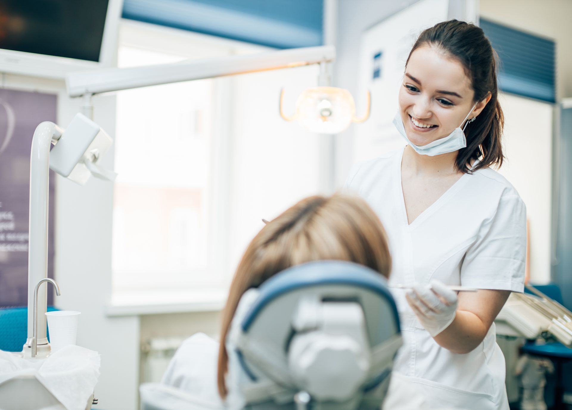 Dentist smiling over a patient in a bright modern clinic, with a dental chair and equipment visible
