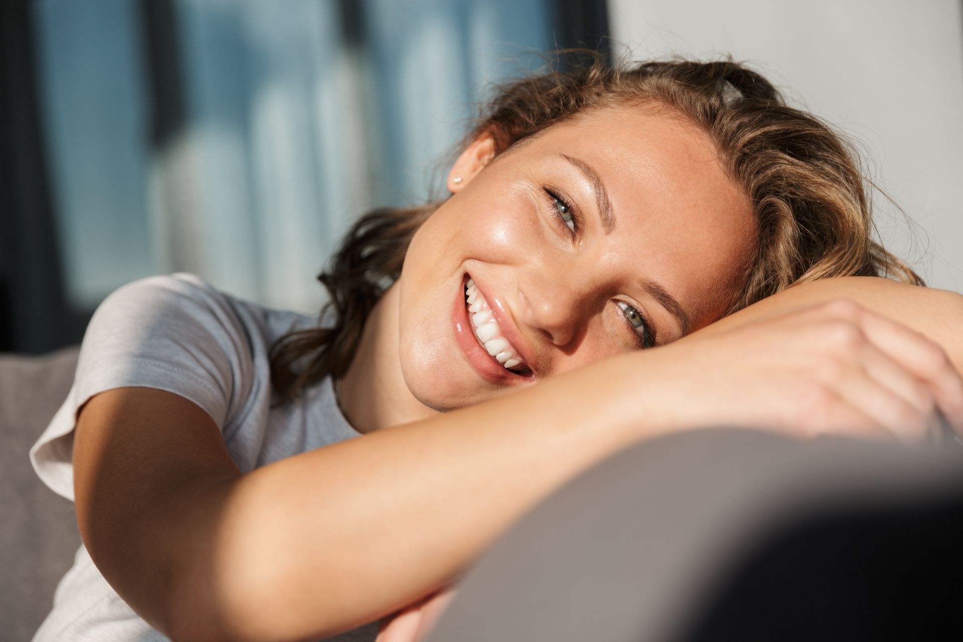 Smiling woman resting her head on her arm in soft sunlight indoors