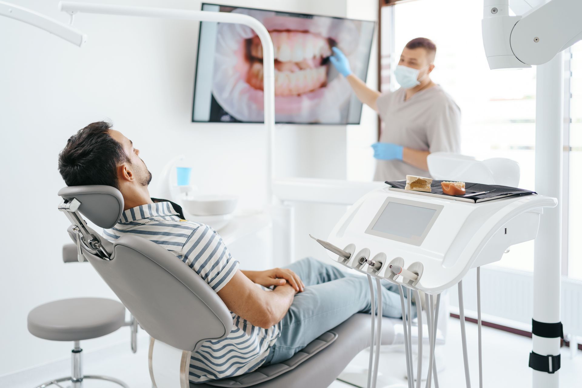 Dentist and patient in a bright clinic, with a dental procedure shown on a wall monitor