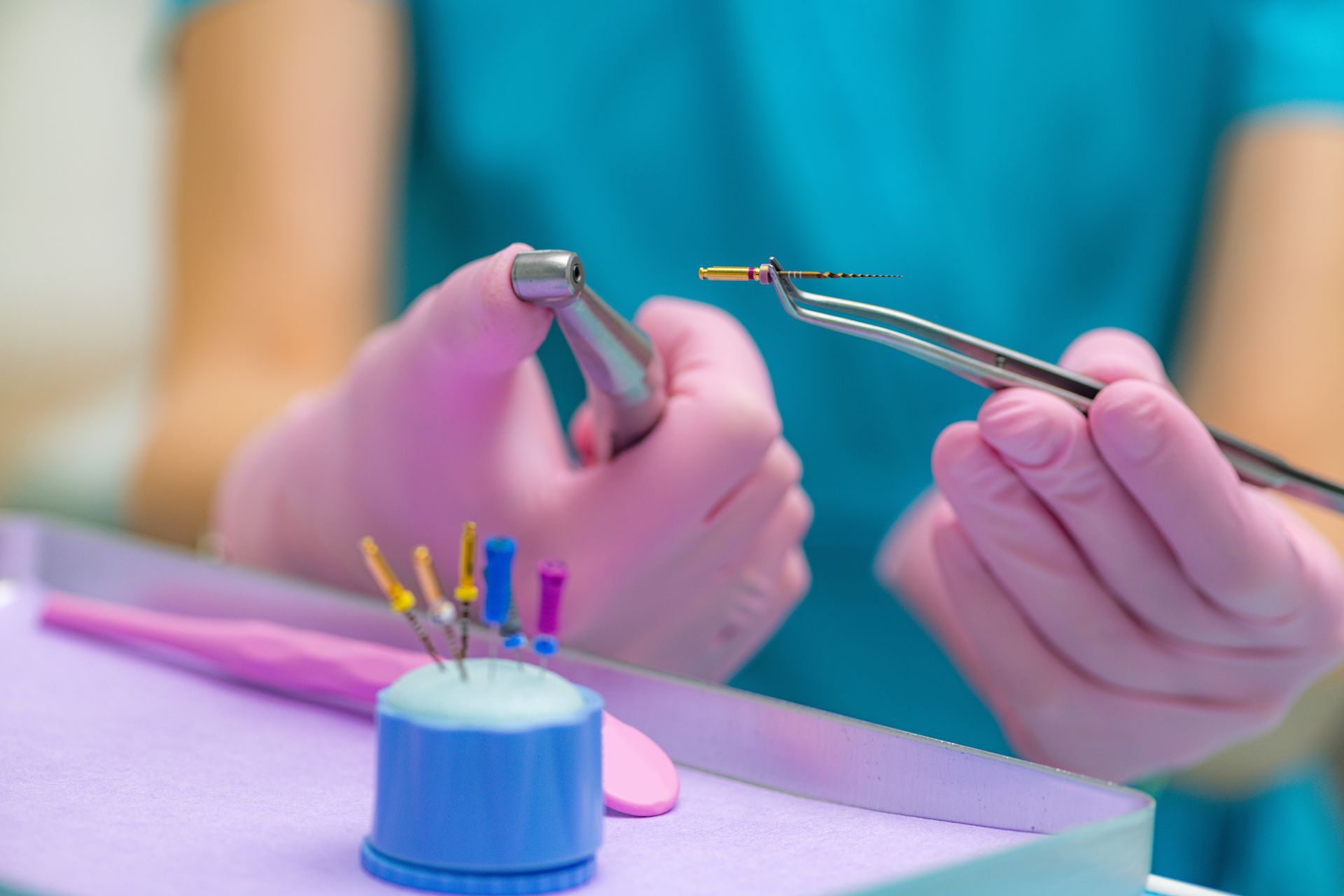 Dental tools held over a model tooth with braces by a person in teal scrubs