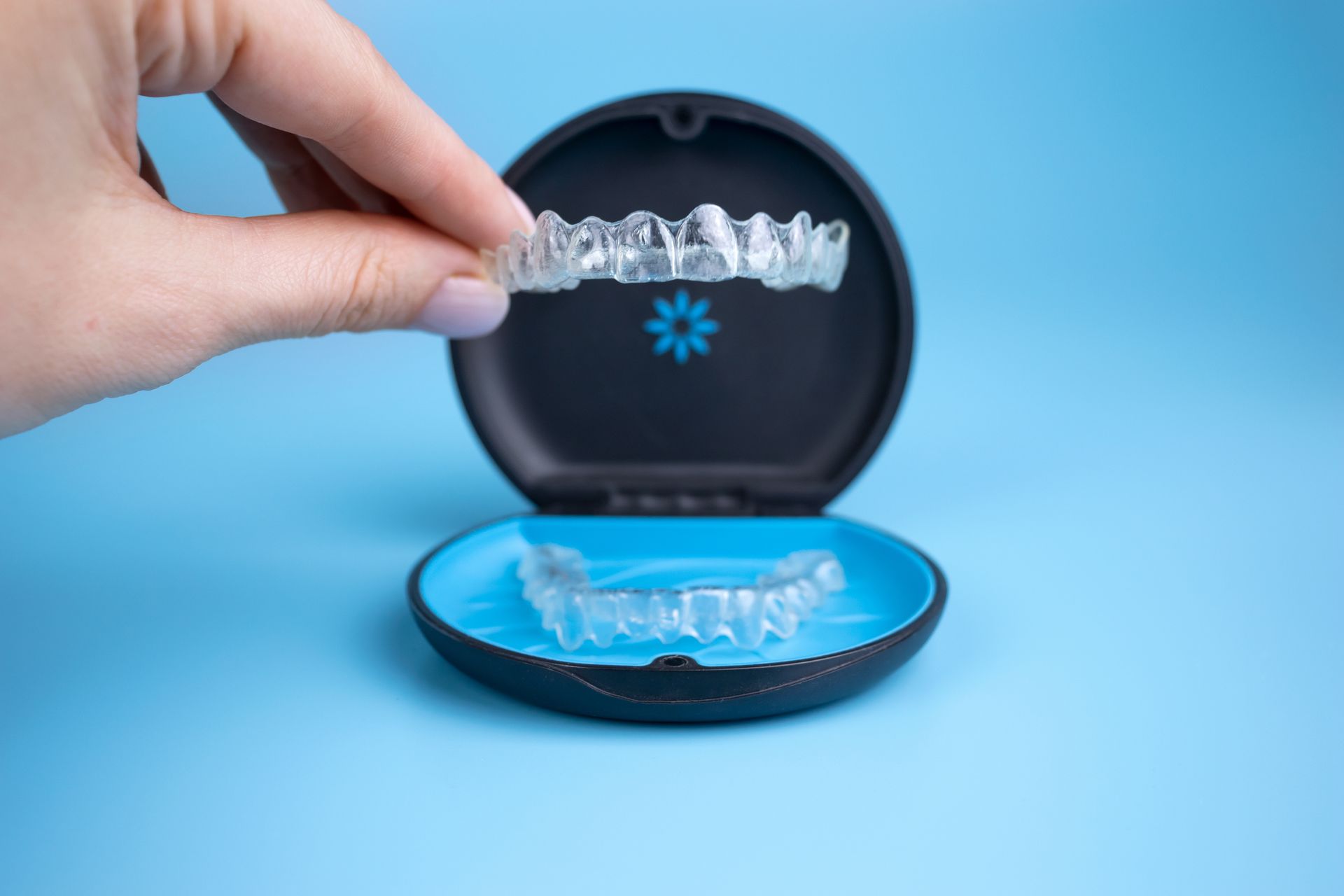 Hand placing a clear aligner into a blue open case on a light blue background